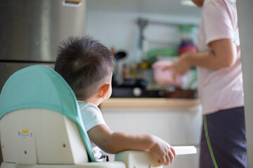 Baby boy sitting on chair waiting mother cooking in kitchen