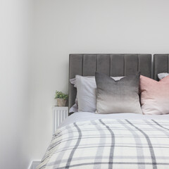 Grey and pink Pillows on bed with plant beside, cover on bed with plant, copy space above.