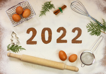 number 2022 on flour on a wooden table in the middle of kitchen utensils and chicken eggs. new year...