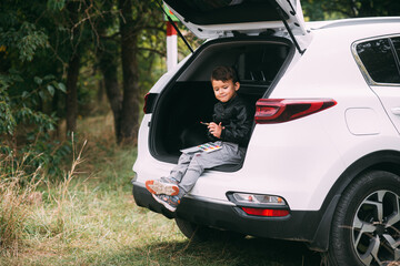 A child is sitting in the trunk of a car SUV or crossover with gouache paints, a car in the autumn...