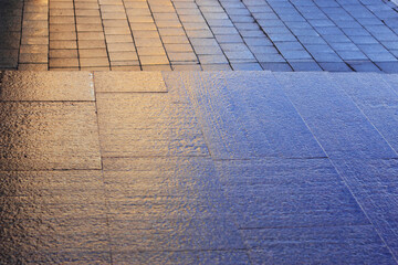 Big city pavement after the rain. Wet granite surface with colorful light. Orange and blue textured background. 