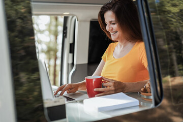 Happy senior woman using computer laptop inside camper mini van - Travel, nature and technology concept - Focus on face