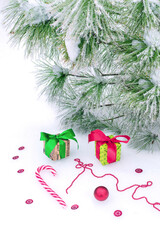 Closeup of green and red ribbon decorated gift boxes, hard candy, red glitter, ball and string of beads on white snow surface near fir tree, tinged with frost. Christmas collection.