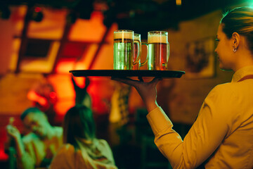 Young waitress serving beer while working in a bar at night.