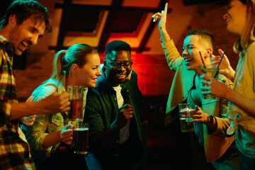 Group of cheerful friends singing karaoke during their night out in a bar. - obrazy, fototapety, plakaty