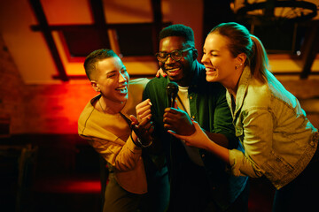 Young happy people having fun and singing karaoke while being in a pub at night.