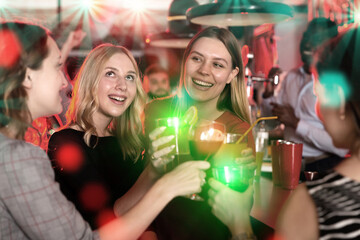 Chatting friends holding cocktails and laughing in nightclub. High quality photo - obrazy, fototapety, plakaty