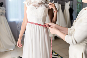 Naklejka premium Seamstress helping bride in wedding salon. Measuring waist by centimeter