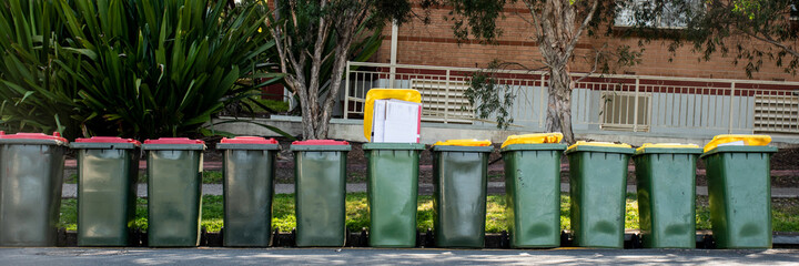 Australian garbage wheelie bins with colourful lids for general and recycling household waste on a street kerbside for council rubbish collection. - obrazy, fototapety, plakaty