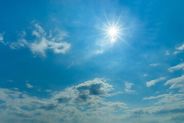 The midday sun shines brightly high in the blue sky. Azure sky with small white clouds on a sunny day. Natural background for weather forecasting, tourism, travel and holydays. Sky only.