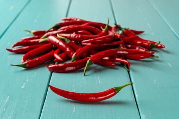 Red hot chili pepper pod in front of raw chilli peppers pile over turquoise wooden table. Whole fresh pungent chiles for cooking. Spicy dishes organic ingredient. Focus on the foreground. Close-up.
