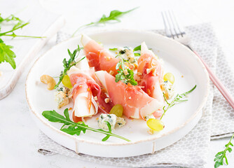 Appetizer with pear, blue cheese and prosciutto ham for holidays on a white plate.