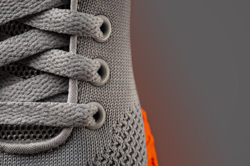 Laced up gray mesh fabric sneakers macro shot. Laced fastening of new orange sole sport shoe close-up. Elastic laces of modern textile trainers for active lifestyle, sport and fitness. Copy space. - obrazy, fototapety, plakaty