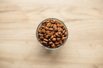 Roasted coffee beans in a glass cup on wooden steel, top view.