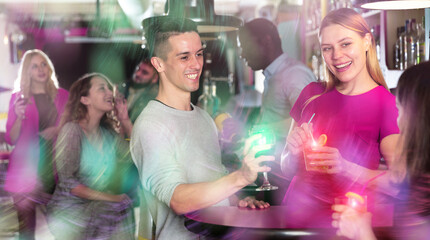 Cheerful young man flirting with women on party and drinking cocktails at nightclub