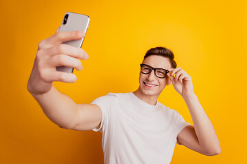 Portrait of cheerful guy hold phone make selfie posing on yellow background
