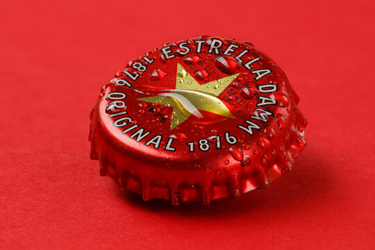 Moscow, Russia, 09.07.2020: Beer Cap with drops on a red background. Red Metal cap beer Estrella Damm, brewed in Barcelona since 1876.