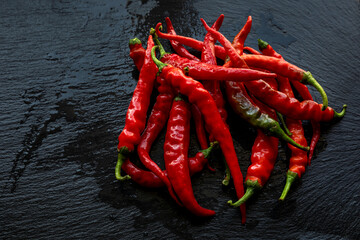 Hot chili heap on wet black slate. Pile of de cayenne long slim peppers in water.