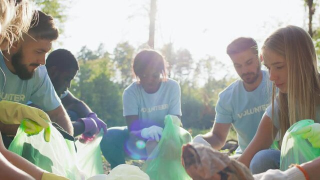 Diverse people volunteers in same t shirts taking plastic trash and putting it to bin bag . Group of multiracial people cleaning public park. Concept of care about nature