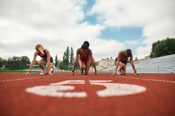 Group of three professional female runners starting the race on track field at the stadium