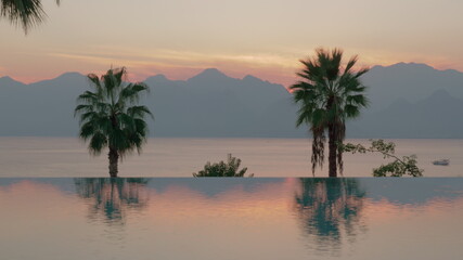 Fototapeta na wymiar Resort scene at sunset Swimming pool with palms, sea and mountains