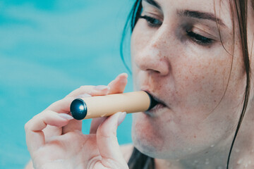 Woman smoking with electronic cigarette. Young woman smoking electronic cigarette in outdoors pool