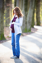 Pregnancy Portrait - Woman Holding Her Belly and Looking at it in a Park