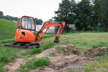 A mini crawler excavator is dripping a trench for laying communications. A mini-excavator is used for digging pits, clearing small areas, and working in the courtyards of residential complexes.