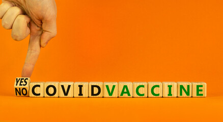 Covid-19 vaccine yes or no symbol. Doctor turns a cube and changes words 'covid vaccine no' to 'covid vaccine yes'. Beautiful orange background, copy space. Covid-19 vaccine and medical concept.