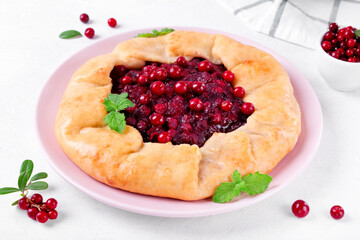Galette with lingonberry on the white table. Sweet pie with forest berries on pastry dough