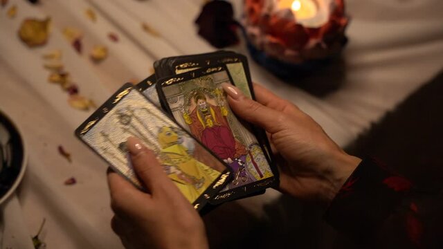 Mystical witch shuffles tarot cards in a dark room by candlelight. Mystic rites and traditions.