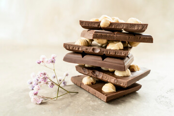 Tower of chocolate pieces with hazelnuts on a white background. Milk chocolate with nuts with a sprig of flowers. Delicious Chocolate for Kids, Holiday, Birthday, Wedding