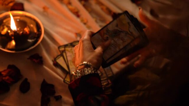 Mystical witch shuffles tarot cards in a dark room by candlelight. Mystic rites and traditions.