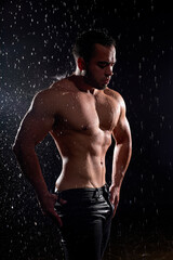 Fototapeta na wymiar Handsome young caucasian man with naked torso posing at camera on black background. Drops of water spread about fitness body. The perfect figure on the background of water splashes. Portrait