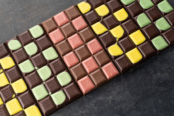 Multicolored fruit chocolate bars on black background. Handmade chocolate with mint, mango, orange, strawberry flavor. Healthy food concept, delicious chocolate sweets for kids, diet, sugar
