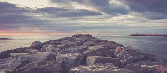 Jetty with water flowing to the ocean. Dramatic cloudy sky at sunrise - panoramic photography - wallpaper © Joseph