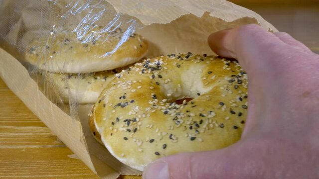 Closeup POV shot of a man&rsquo;s hand taking a fresh Persian barbari bread (yeast leavened Iranian flatbread), in a bagel shape, topped with nigella and sesame seeds, from four in a paper packet.