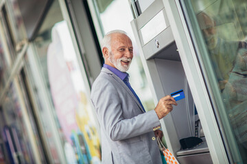 Senior man using bank cash machine - obrazy, fototapety, plakaty