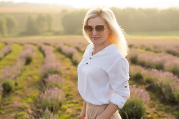 Fototapeta na wymiar Beautiful young healthy woman with a white dress running joyfully through a lavender field holding a straw hat under the rays of the setting sun