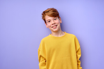 Young emotional handsome boy standing on purple studio background. Human emotions, facial expression concept. Cute caucasian boy in yellow casual shirt looking at camera smiling, diligent and shy