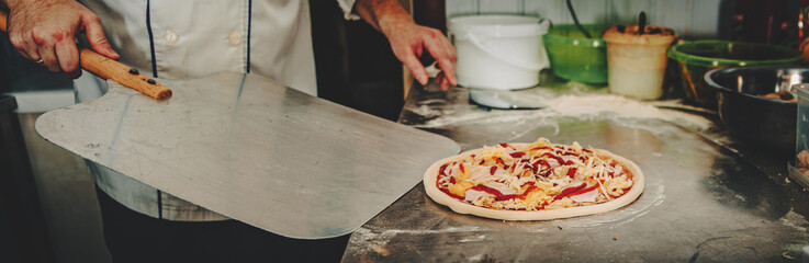 Closeup hand of chef baker making pizza at kitchen. Put on landing shovel and send it to the oven.