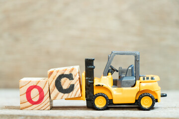 Toy forklift hold letter block C to complete word OC (Abbreviation of opportunity cost or original content, character) on wood background