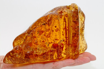 Large piece of transparent yellow amber in the palm of your hand on a light background. Amber texture with insects and patterns inside. Sunstone in the girl's hand. Material for making jewelry. Copal