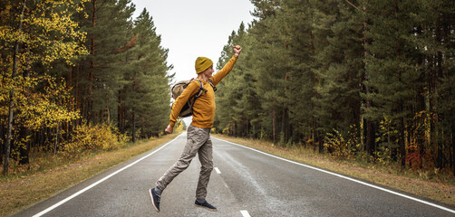 Traveler with a backpack on a road along the forest is jumping with his arms outstretched. Concept of freedom