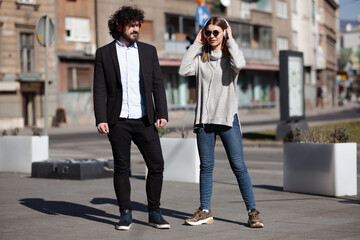 Naklejka premium Business colleagues listening to music together with headphones after work. Friends walking outdoors in an european city.