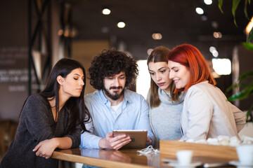 Four friends sitting at a cafe bar having a conversation looking at tablet. Positive face expressions.
