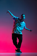 Vertical portrait of young man dancing hip-hop isolated over gradient pink purple background in...
