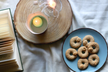 Plate with cookies, open book, lit candles and fairy lights. Hygge at home. Flat lay.