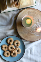 Plate with cookies, open book, lit candles and fairy lights. Hygge at home. Flat lay.