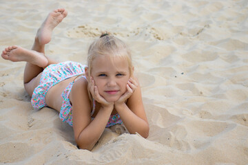 little european girl with blond hair and blue eyes sunbathes on a sandy beach, summer family vacation with children at the sea